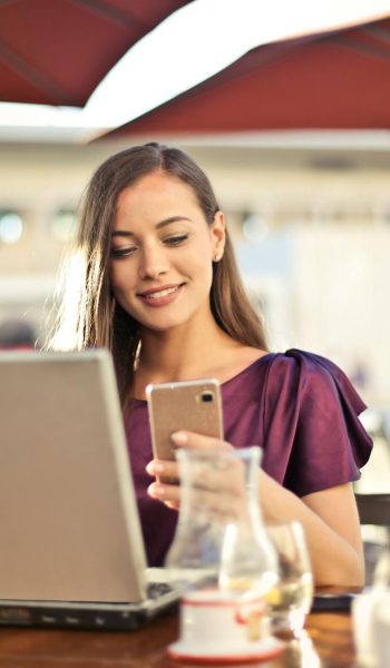 Woman enjoying remote work at a café, using a laptop and smartphone.