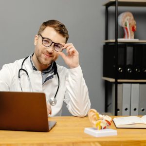 doctor-sitting-at-desk-with-laptop-e1738346796933.jpg
